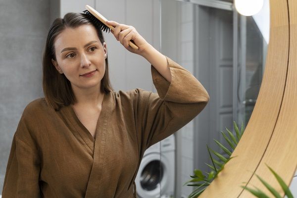 donna che si guarda nello specchio e si pettina, massaggio cuoio capelluto per crescita