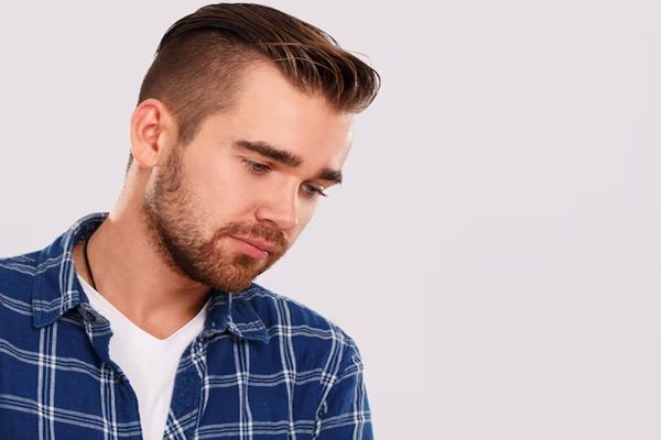 giovane uomo caucasico in camicia blu che guarda a terra con tristezza. Disimulare un trapianto di capelli 