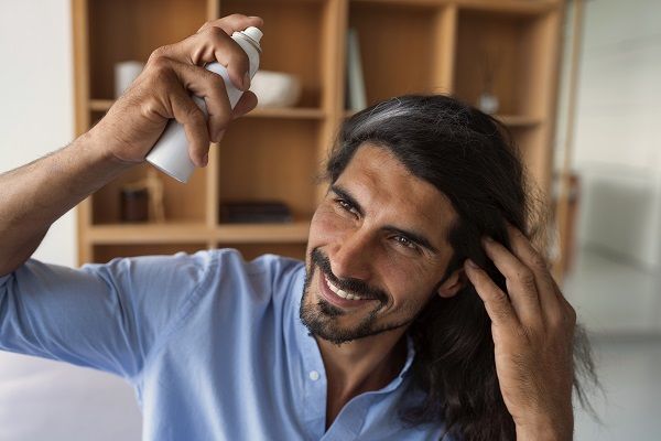 Uomo con i capelli lunghi che usa la lacca sui suoi capelli lunghi