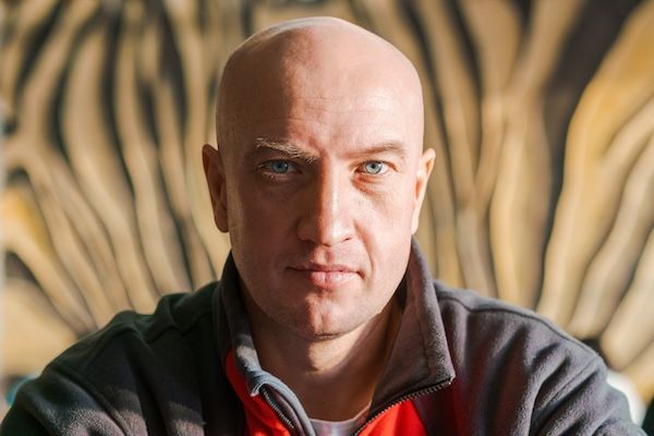 Ritratto in primo piano di un uomo calvo con occhi azzurri che indossa una felpa sportiva