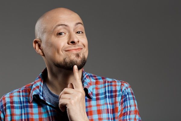 Ritratto di un uomo bello, pensieroso e allegro con una camicia a quadri che sorride alla fotocamera su uno sfondo grigio
