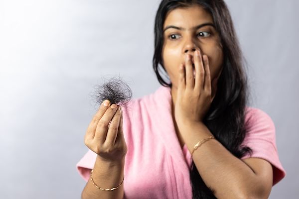 Messa a fuoco selettiva sui capelli caduti tenuti in mano da una donna indiana preoccupata, su uno sfondo bianco.