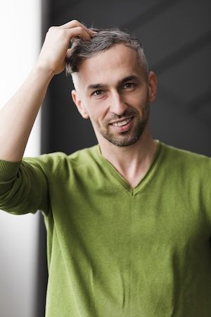 Uomo con una camicia verde che si sistema i capelli.