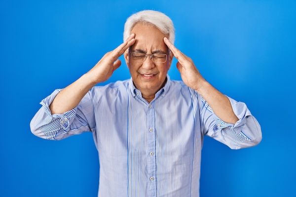 Uomo anziano ispanico con occhiali, con mal di testa dovuto allo stress