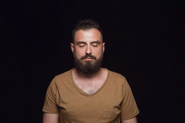 Primo piano del ritratto di un uomo giovane isolato. Emozioni reali del modello maschile con gli occhi chiusi. Pensieroso. Concetto di espressione facciale, natura umana ed emozioni.