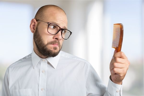Uomo calvo che guarda un pettine con un'espressione confusa.