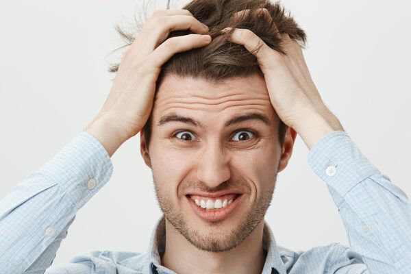 Giovane con un cipiglio frustrato su fondo bianco che tira i suoi capelli - Uomini con linea frontale sfuggente.