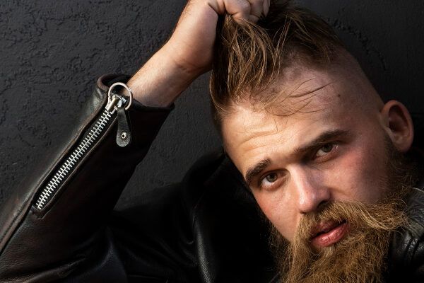 Uomo rocker in posa per la macchina fotografica mentre si accarezza i capelli con un finto taglio a occhio di falco.