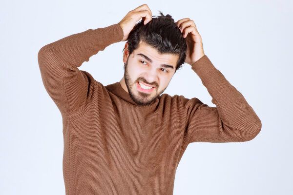 Giovane con prurito al cuoio capelluto ed espressione preoccupata - Cosa c'entra il testosterone con la caduta?