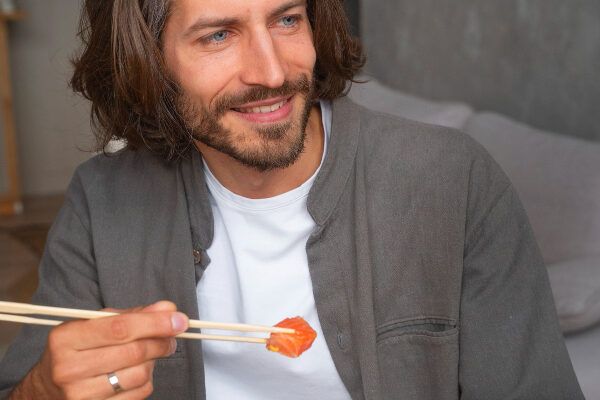 Uomo sorridente con le bacchette in mano contenente un pezzo di salmone.