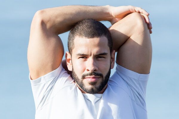 Uomo con capelli rasati e flanella bianca che si allunga al sole - Estate e calvizie.