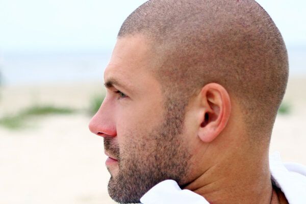 Giovane con capelli rasati sulla spiaggia guardando l'orizzonte - Estate e calvizie