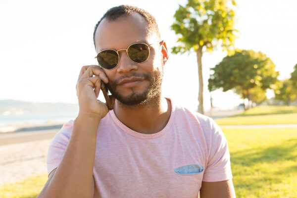 Giovane con la pelle scura che risponde al telefono mentre riposa sull'erba.