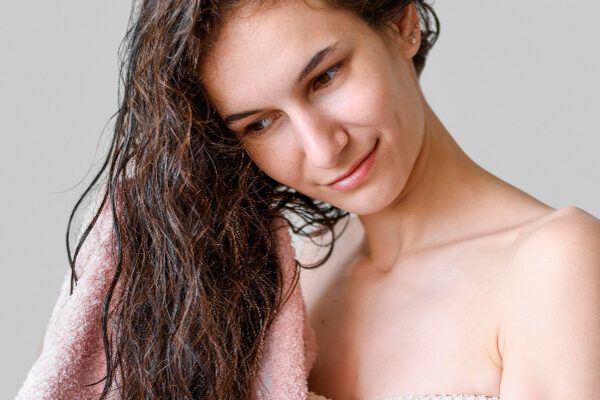 Donna magra dalla pelle chiara che si asciuga i capelli bagnati con un asciugamano rosa che tiene tra le mani.