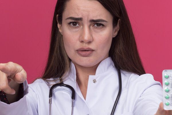 Giovane dottoressa con lo stetoscopio che punta verso la telecamera che mostra un blister di pillole.