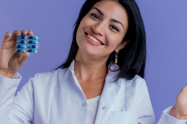Giovane dottoressa con un camice bianco che mostra su uno sfondo viola il blister di pillole che ha tra le mani che esprimono la soluzione - Spironolattone per l'alopecia.