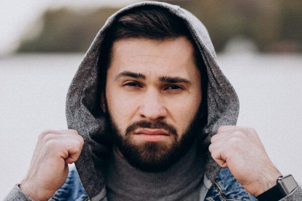 Bell'uomo barbuto con maglione di jeans blu e felpa con cappuccio che cammina all'aperto.