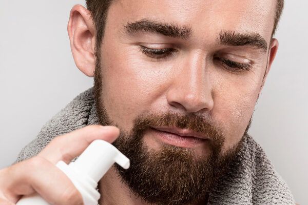 Uomo dagli occhi chiari con barba e crema da barba tra le mani.