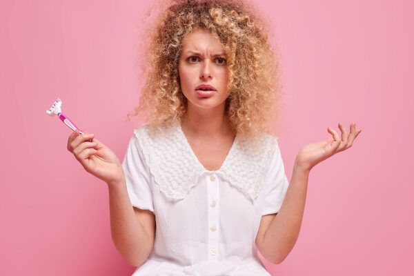 Donna adulta con capelli ricci biondi con rasoio in mano ed espressione scontenta - L'irsutismo ormonale.