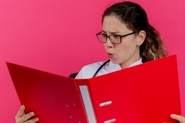 Dottoressa con gli occhiali che esamina un referto medico, sorpresa da ciò che legge.