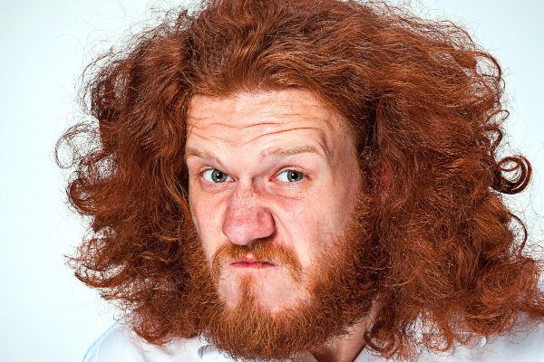 Uomo dai capelli rossi con capelli lunghi e bigodini con un'espressione lamentosa o insoddisfatta - Cos'è l'ipertricosi.