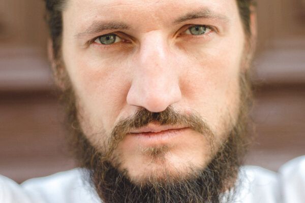 Uomo attraente con barba lunga e occhi verdi biondi che fissano la telecamera.