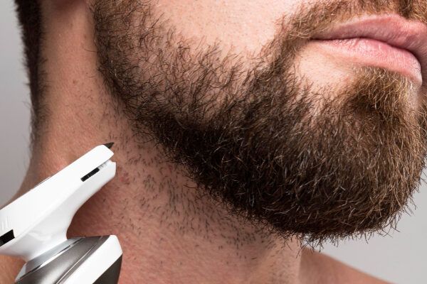 Primo piano estremo di un uomo che si taglia la lunga barba con un rasoio speciale.