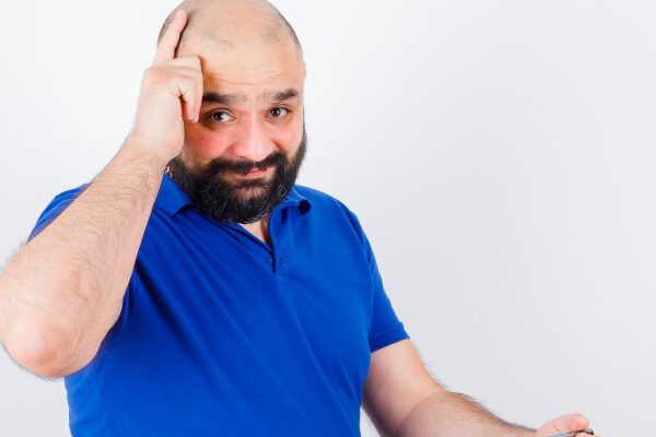 Uomo adulto con i baffi che si tocca il cuoio capelluto calvo con espressione inquieta - Rischio di rigetto nel trapianto.