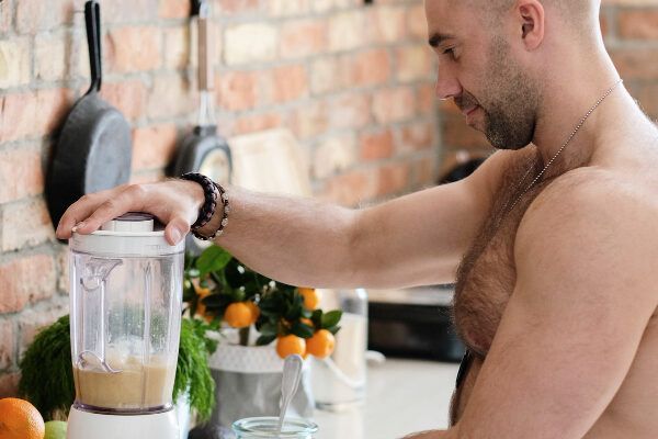 Uomo muscoloso senza maglietta in cucina che prepara un frullato nel frullatore- Frullati proteici e calvizie