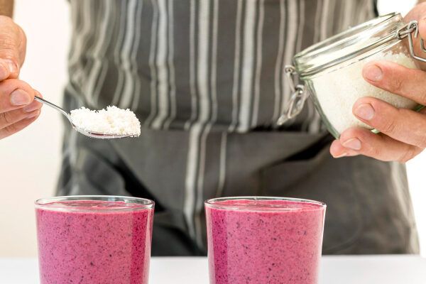 Uomo che aggiunge un ingrediente mancante al suo frullato di frutta viola.