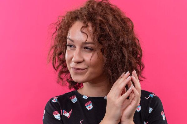 Giovane donna truccata adulta con i capelli corti con riccioli e una camicetta sorridente che guarda di lato mentre gioca con i capelli - Slugging provoca la caduta.