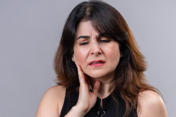 Donna anziana che si tocca il collo con l'espressione del dolore interno.