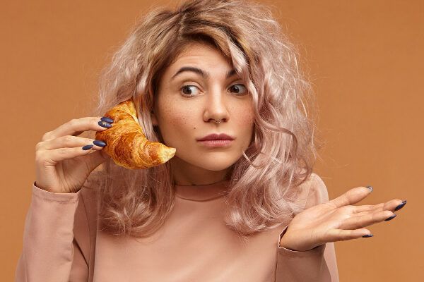 Giovane donna con i capelli tinti che tiene un croissant con la mano, facendo riferimento a tenere in mano un telefono, esprimendo indifferenza - Alimenti che causano la caduta.