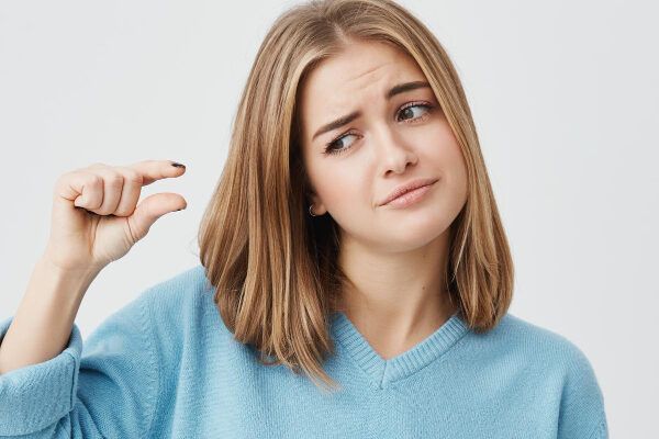 Giovane donna dai capelli corti e dai riflessi biondi accigliata mentre si guarda la mano con cui si riferisce a qualcosa di molto piccolo - Alimenti che causano la caduta.