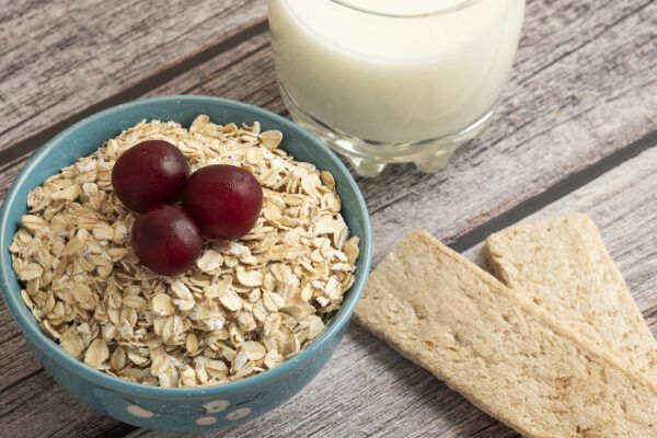 Mesone con una ciotola di vetro contenente avena e uva accompagnato anche da un paio di biscotti e da una bevanda a base di latte.