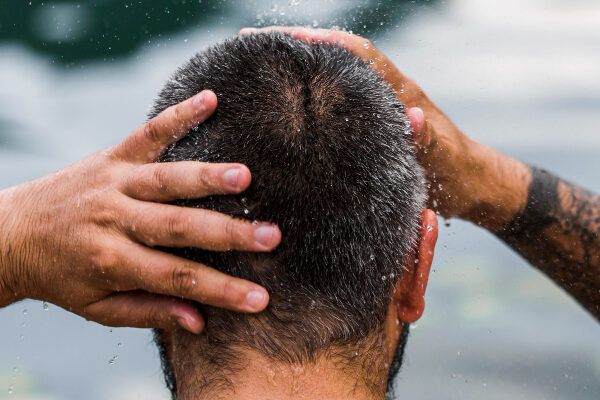 Uomo con capelli rasati e profilo basso che si massaggia il cuoio capelluto davanti a un lago.