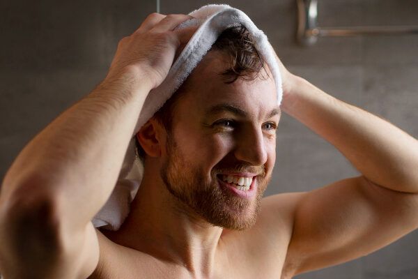 Giovane con occhi chiari e capelli che si massaggia il cuoio capelluto con un asciugamano quando esce dalla doccia in bagno.