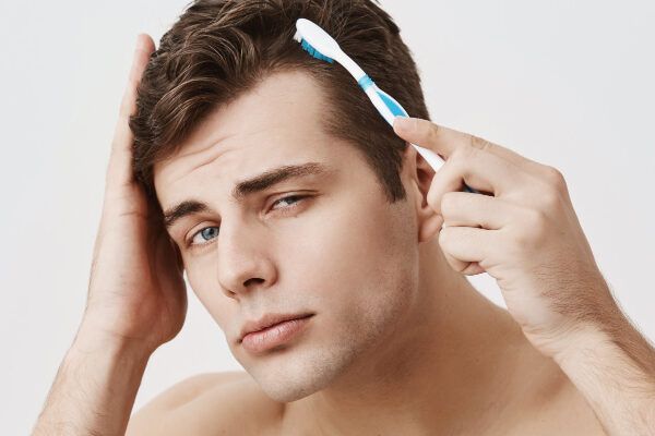 Giovane ragazzo con i capelli curati che li spazzola mentre posa davanti alla telecamera su uno sfondo bianco con un'espressione seducente.