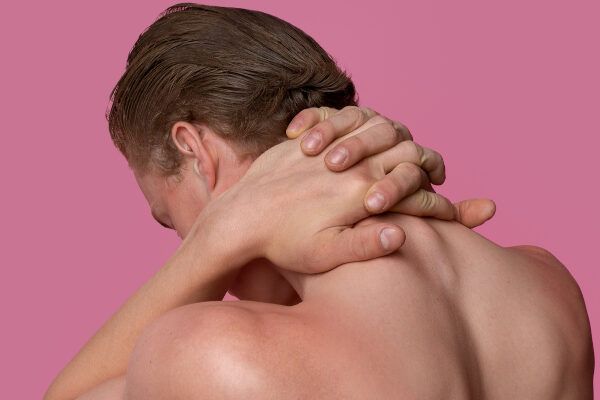 Giovane donna con la schiena nuda in posa su sfondo rosa mentre tiene il collo avvilito.