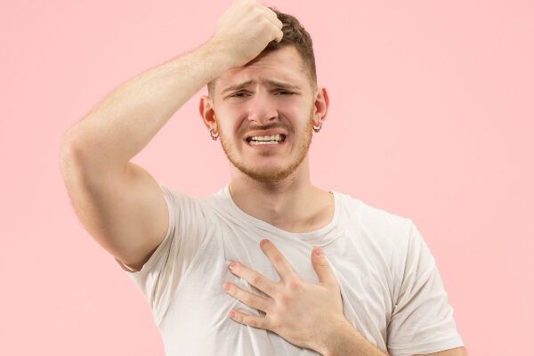 Uomo con barba e capelli castani che si prende i capelli con un'espressione preoccupata e spaventata mentre si tocca il petto.