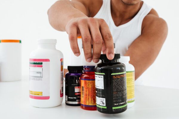 Uomo bodybuilder muscolare che seleziona meticolosamente un farmaco tra diverse bottiglie.