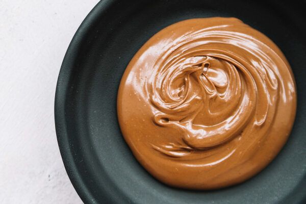 Ciotola nera ripiena di crema spalmabile al cioccolato al latte e nocciole.