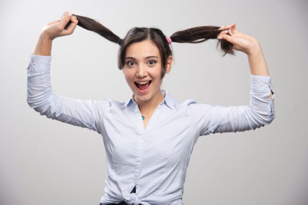 Ragazza con due trecce che le prendono i capelli con un grande sorriso di sorpresa - Accessori per capelli dannosi.