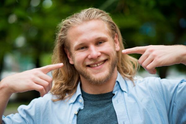 Uomo con capelli lunghi con riflessi e tono biondo che sorride alla telecamera.