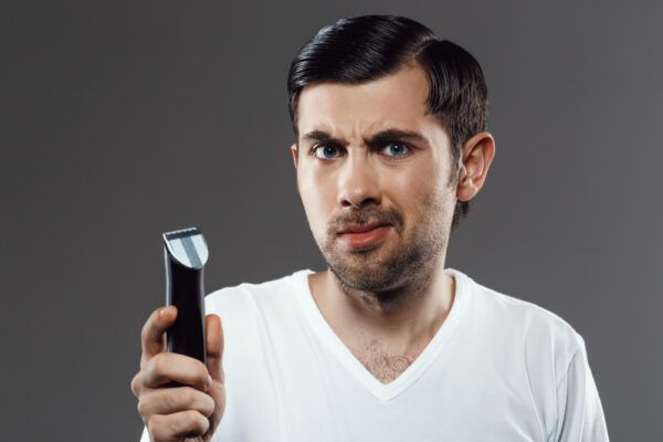Uomo con i capelli stirati e l'espressione confusa mentre tiene un rasoio tra le mani.