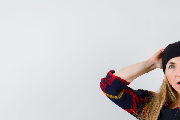 Donna con lunghi capelli gialli che si tiene la testa toccandosi il cappello sorpresa - Berretto fa cadere i capelli? 