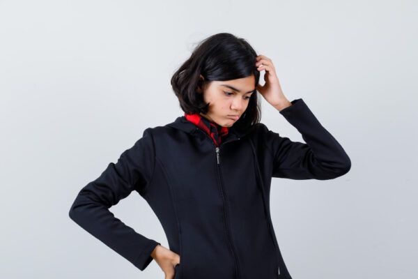 Giovane ragazza con una posa premurosa che guarda a terra mentre indossa un abito natalizio.