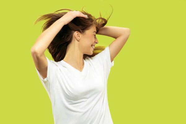 Giovane ragazza sorridente in posa su uno sfondo verde mentre si tocca il cuoio capelluto e scuote i capelli.