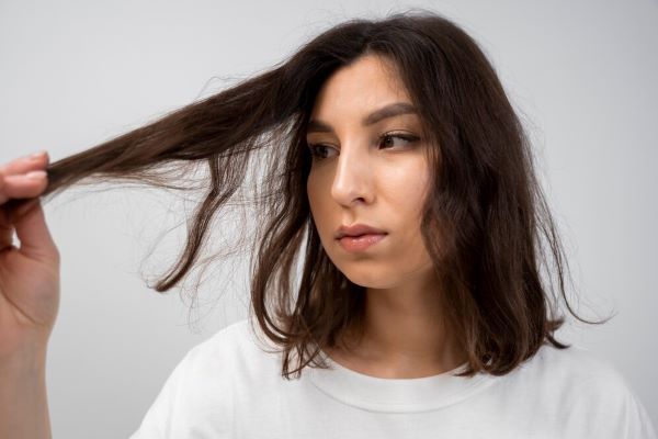 Ragazza che guarda i suoi capelli con un gesto preoccupato