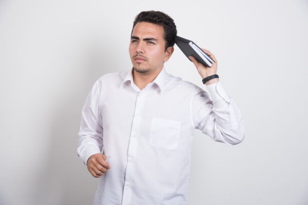 Un ragazzo guarda pensieroso di lato mentre tiene in mano un quaderno e lo appoggia sulla testa.